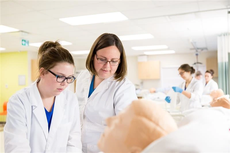 Experience at Oulton College our Licensed Practical Nursing Program. Image has an Oulton College Practical Nursing Student in the Nursing Lab, while students are completing there Practical during a lesson.