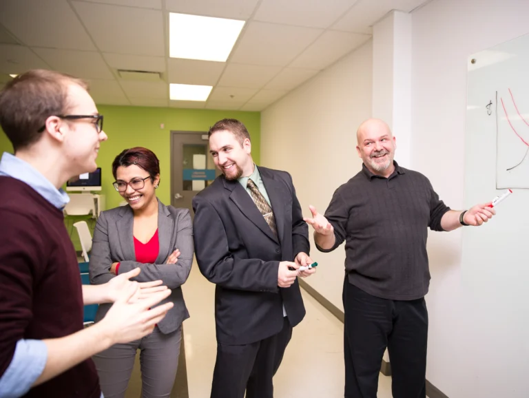 Business administration students at Oulton College. Three students stitting around a table with an instructor teaching Business administration and Business managemnet concepts, as part of their Associates Degree in Business Administration.